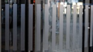 Grey vertical glass slats partly obscuring a blurred lit interior behind them.